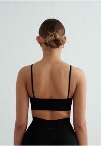 Zwarte sportbeha met dunne banden, textuurstof en logodetail, gecombineerd met hoge zwarte legging met een V-vormige tailleband.