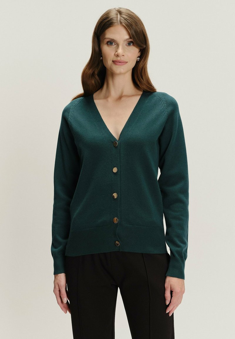 Dunkelgrüner Cardigan aus weichem Material, mit V-Ausschnitt, langen Ärmeln, Knopfverschluss und geripptem Saum mit dekorativen Knöpfen.