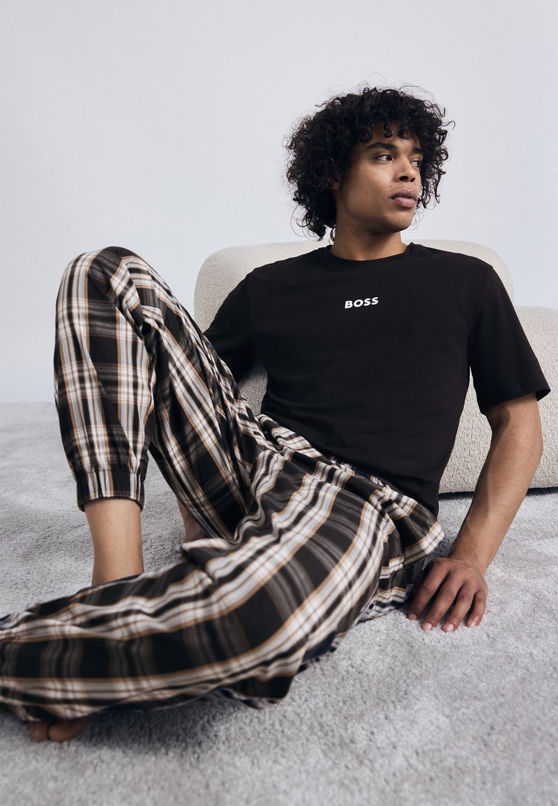 Tricou negru cu mânecă scurtă, inscripționat cu textul "BOSS", asortat cu pantaloni de pijama în carouri, în nuanțe de maro, crem și albastru, strânsi la glezne.