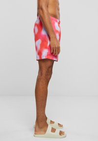 Krátke plavky majú červený a ružový tie-dye vzor, elastický pás a ľahký materiál. Šľapky sú svetlo béžové s dvojitým popruhom.