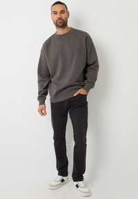 Grå sweatshirt med ribbede manchetter og kant, parret med sorte jeans og hvide sneakers med sorte accenter. Stående stilling mod en neutral baggrund.