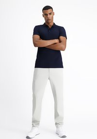 Granatowa koszulka polo z kołnierzykiem, z trzema guzikami; zestawiona z jasnoszarymi spodniami i białymi trampkami. Gładki materiał, dopasowany krój.