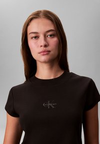 T-shirt nera a coste con collo alto e maniche corte, con un piccolo logo Calvin Klein stampato a contrasto vicino al centro.
