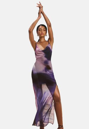 Maxi dress in sheer fabric featuring a gradient of purples and pinks. Spaghetti straps, side slit, and draped design for a flowing silhouette.