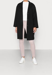 Svartullkappa med breda slag och fyra knappar, kombinerad med ljusrosa slim fit-jeans och vita sneakers. Enkel, minimalistisk design.