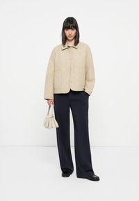 Beige quiltet jakke med en firkantet design, store lappe lommer og kragehalser. Kombinert med marineblå vide bukser og en liten lys veske.