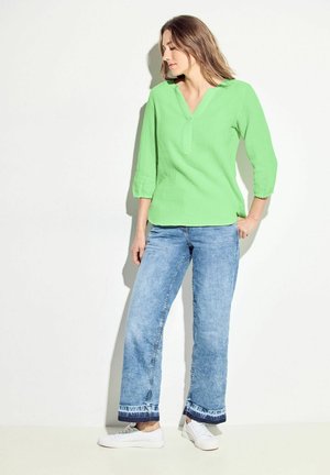 Maglietta verde con scollo a V, maniche a tre quarti, tessuto testurizzato. Abbinata a jeans azzurri dritti, taglio corto con orlo sfrangiato. Sneakers bianche.