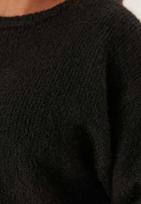 Maglione nero lavorato a maglia con un tessuto morbido e testurizzato, caratterizzato da un collo rotondo e un design ampio e rilassato.