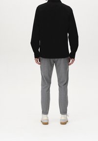 Black long-sleeve shirt with button cuffs, paired with light gray tapered pants. The outfit is complemented by light shoes with a gum sole.