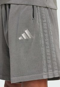Light gray athletic shorts made of cotton blend fabric. Features include an elastic waistband, pockets, and a textured stripe design on the sides.