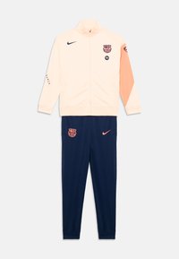 Nike Barcelona trainingspak in licht perzik en marineblauw. Bevat een gezoomde jas met logo, broek met elastische tailleband en contrasterende mouwdetails.