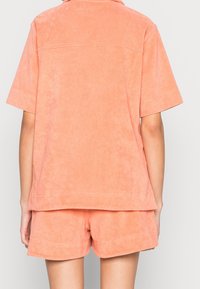 Ensemble de haut et de shorts à manches courtes de couleur pêche en tissu doux et texturé. Le haut a un col, et les deux pièces présentent de simples détails de couture.