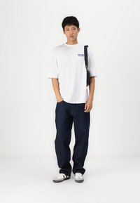 Hvid kortærmet t-shirt med teksten "DELIGHT", parret med mørkeblå løse jeans og hvide sneakers med sorte detaljer.