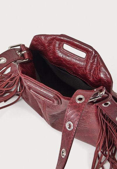 Sac à main en cuir rouge texturé avec œillets argentés, bandoulière réglable, poignée découpée et détails à franges, présenté ouvert avec une doublure intérieure noire.