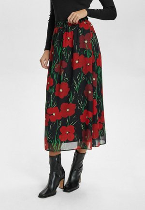 Svart blommig kjol med stora röda blommor och gröna stjälkar, med elastisk midja, kombinerad med svarta ankelstövlar.