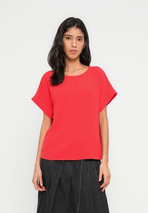 Haut rouge à manches courtes avec un col rond et une finition texturée, associé à une jupe plissée foncée.