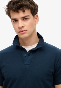 Polo shirt blu navy realizzato in morbido cotone, con colletto a bottoni e maniche corte, caratterizzato da una consistenza sottile e una vestibilità sagomata.