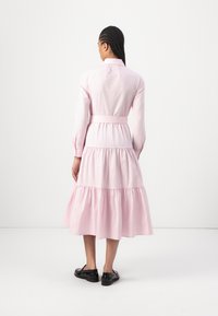 Vestido longo de mangas compridas em rosa claro, com saia em camadas, cintura cintada e gola com botões. Tecido suave com um brilho subtil.