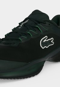 Μαύρο αθλητικό παπούτσι Lacoste με πράσινες λεπτομέρειες, μαύρα κορδόνια και λευκό κεντητό λογότυπο κροκόδειλου στο πλάι.