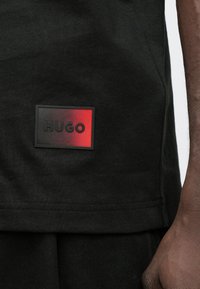 Μαύρο βαμβακερό t-shirt με ορθογώνιο λογότυπο HUGO σε διαβάθμιση από κόκκινο σε μαύρο. Λείο ύφασμα με στρογγυλή λαιμόκοψη και κοντά μανίκια.