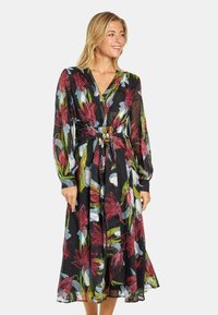Vestido de manga larga con diseño envolvente que presenta un fondo negro con patrones florales rojos y azules. Tejido ligero y semitransparente con un detalle de cinturón atado en la cintura.