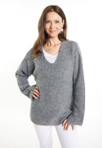 Pulover gri texturat din tricot, cu guler în V și mâneci lungi, având o croială lejeră și un model cu nervuri. Purtați peste o bluză albă.