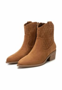 Botas de tobillo de ante en tono arena con punta afilada y tacón bajo, con patrones de flores recortados y una cremallera lateral para mayor comodidad al ponérselas.
