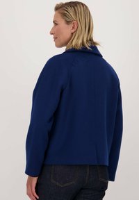 Navyblauwe jas met een kraag, op maat gemaakt ontwerp en lange mouwen. Beschikt over een rugventilatie en een gladde textuur. Draag het over een donkere spijkerbroek.