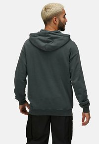 Grå hoodie med huva och ribbade muddar, tillverkad av mjukt material. Har en avslappnad passform och är kombinerad med svarta cargobyxor.