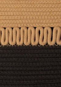 Spleciony dywan z kontrastującą górną częścią w kolorze beżowym i dolną częścią w czerni, z teksturowanymi wzorami i falistym brzegiem.