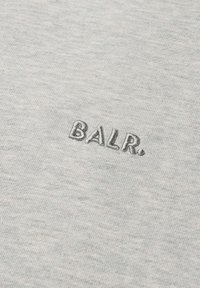 Harmaa kangas, jossa on teksturoitu pinta, ja jossa on brodeeratut kirjaimet "BALR." hieman tummemmalla sävyllä. Yksinkertainen ja siisti muotoilu.