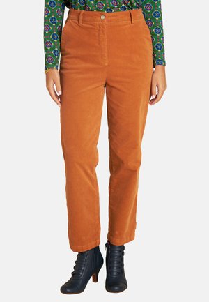 Kordhosen in einem warmen Orangeton, mit geradem Bein, vorn mit Knopfverschluss und kombiniert mit schwarzen, geschnürten Stiefeletten mit Absatz.