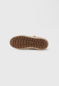 Brązowa gumowa podeszwa beżowego buta casualowego z głębokim bieżnikiem i brandingiem "GLOBE" na środku podeszwy.