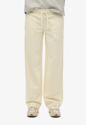 Kremowe dresy z miękkiego materiału, z elastycznym pasem i szerokimi nogawkami. W połączeniu z beżowymi butami sportowymi w deseń.