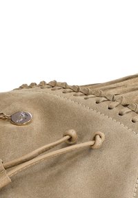 Beżowa torebka z zamszu z plecionymi akcentami, okrągłym metalowym zawieszką i zaciąganym zamknięciem. Gładka tekstura z kontrastującymi detalami ściegów.