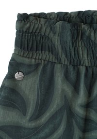 Taille élastique sur un short vert foncé avec un motif abstrait de feuilles noires et une petite plaque ronde en métal de la marque sur le côté.