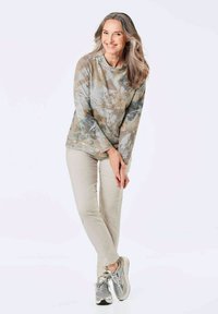 Lichte, langmouwige top in een gedempt blauw en beige bloemenpatroon, gecombineerd met lichte beige broeken en grijze sneakers.