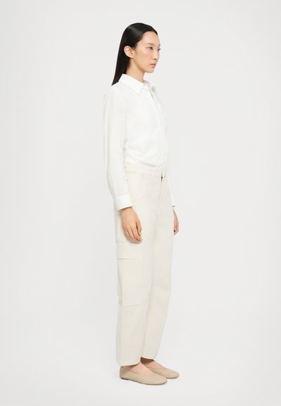 Witte lange mouwen shirt met knoopsluiting, lichtbeige hoge taille broek met zijzakken en nude instappers.