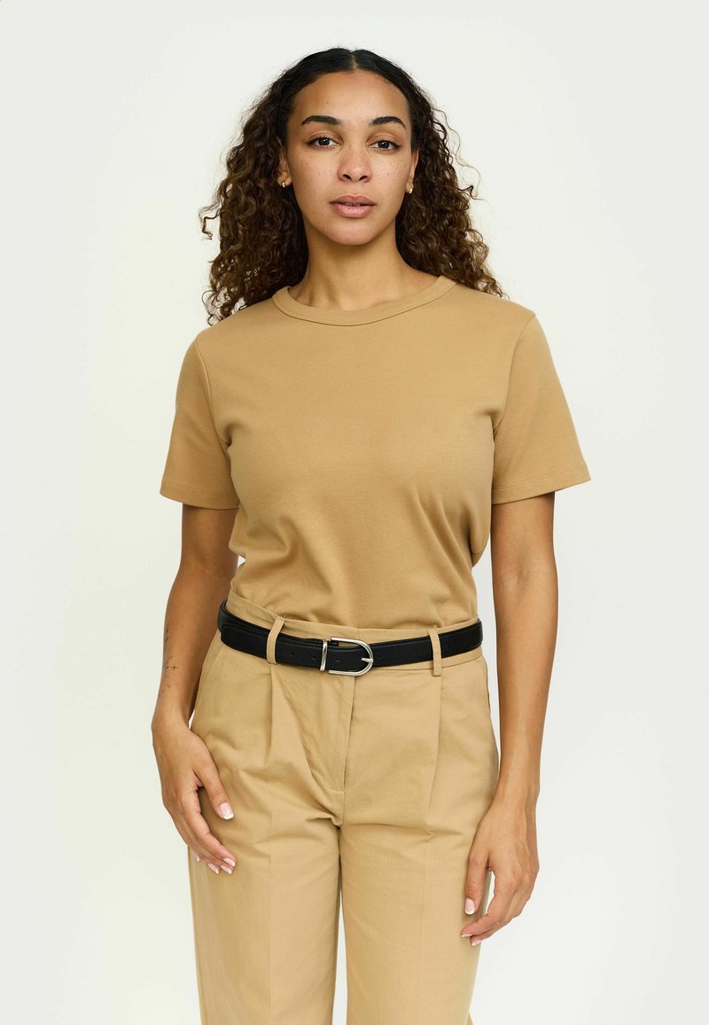 Kārtējas piedurknes, apaļā kakla bežs T-krekls, izgatavots no kokvilnas, apvienots ar gaismas bežām biksēm un melnu jostu ar sudraba sprādzi.