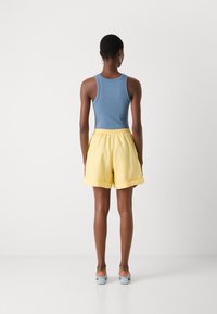 Blue ribbed tank top paired with yellow shorts, featuring an elastic waistband, loose fit, and rolled cuffs, worn with light blue heeled sandals.