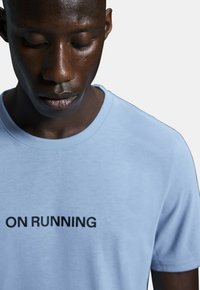 Light blue cotton t-shirt featuring a crew neck and short sleeves, with bold black text "ON RUNNING" centered on the front.
