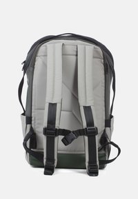 Grijze stoffen rugzak met een donkergroene bodem. Heeft gewatteerde schouderbanden, een verticale quiltontwerp en meerdere verstelbare gespen.