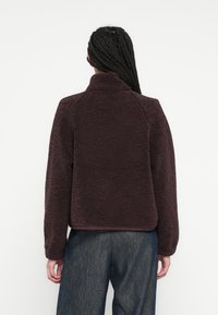 Weiche Fleece-Jacke in Burgunderrot mit hohem Kragen, langen Ärmeln und geradem Saum. Verfügt über eine weiche Textur und Raglanärmel.