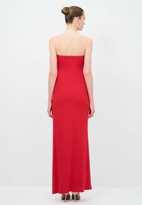 Červené, bezramínkové, přiléhavé maxi šaty s hladkým povrchem. Šaty splývají až na zem, předvádějí štíhlou siluetu a minimalistický design.