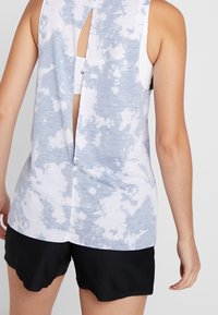 Débardeur à motif tie-dye bleu et blanc, avec un dos en forme de goutte d'eau et une coupe ample. Associé à un short de sport noir.