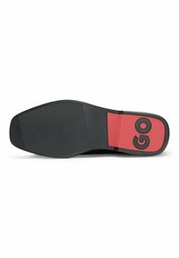Suola di scarpa nera con superficie testurizzata; presenta un accento in gomma rossa con la scritta "GO". Bordo liscio e design minimalista.