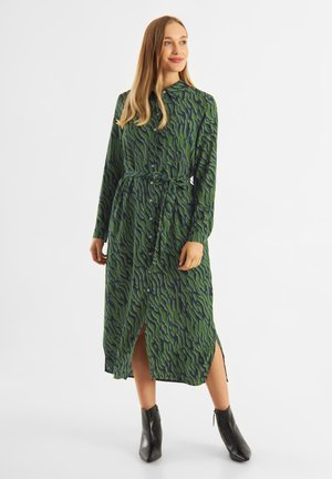 Green dress with wave pattern, long sleeves, button-down front, and belt at waist; features side slits. Worn with black ankle boots.