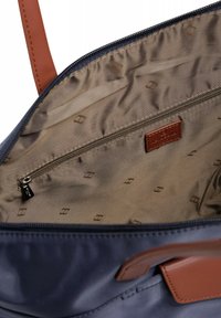 Interno di una borsa blu navy con tasca con zip, foderato in beige e con motivi sottili. Completata con dettagli in pelle marrone e cuciture.