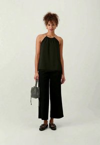Top negro tipo halter con un corte holgado, combinado con pantalones negros de pierna ancha. También cuenta con un pequeño bolso de mano con estampado y zapatos planos negros.