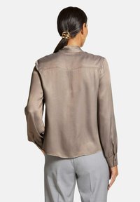 Lange mouwen, taupe satijnen blouse met een gladde textuur, knoopmanchetten en een licht getailleerde pasvorm, gecombineerd met lichtgrijze broek.